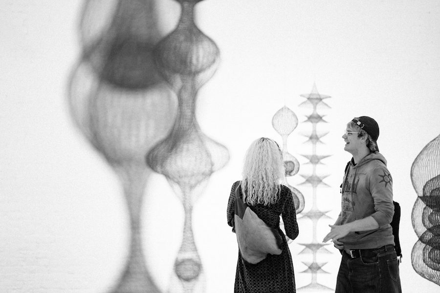 Two people viewing a series of hanging sculptures made of looped wire, in organic round shapes.