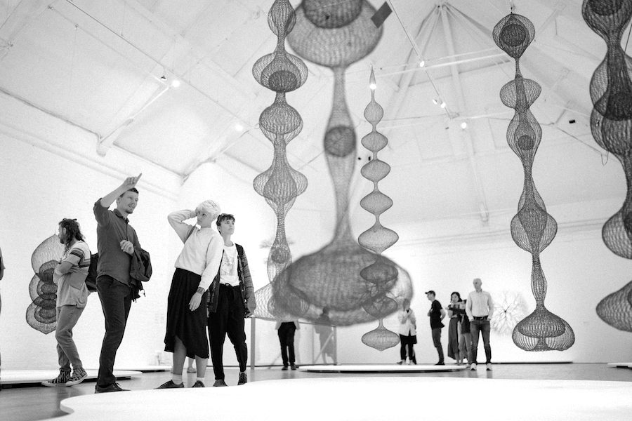 Multiple people viewing hanging wire sculptures in a large gallery space