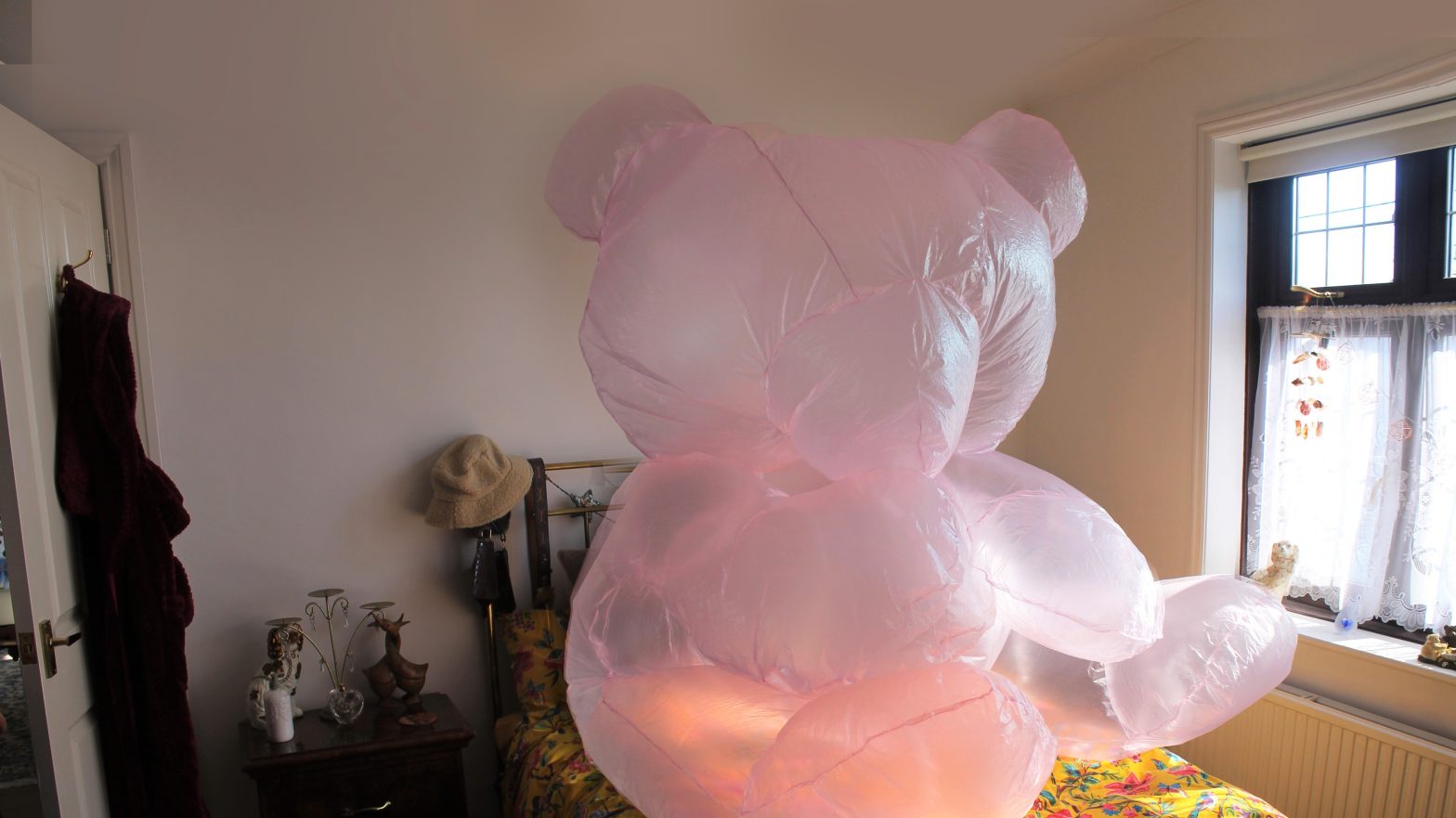Photo of a messy bedroom with a large pink blow-up teddybear placed on a double bed.