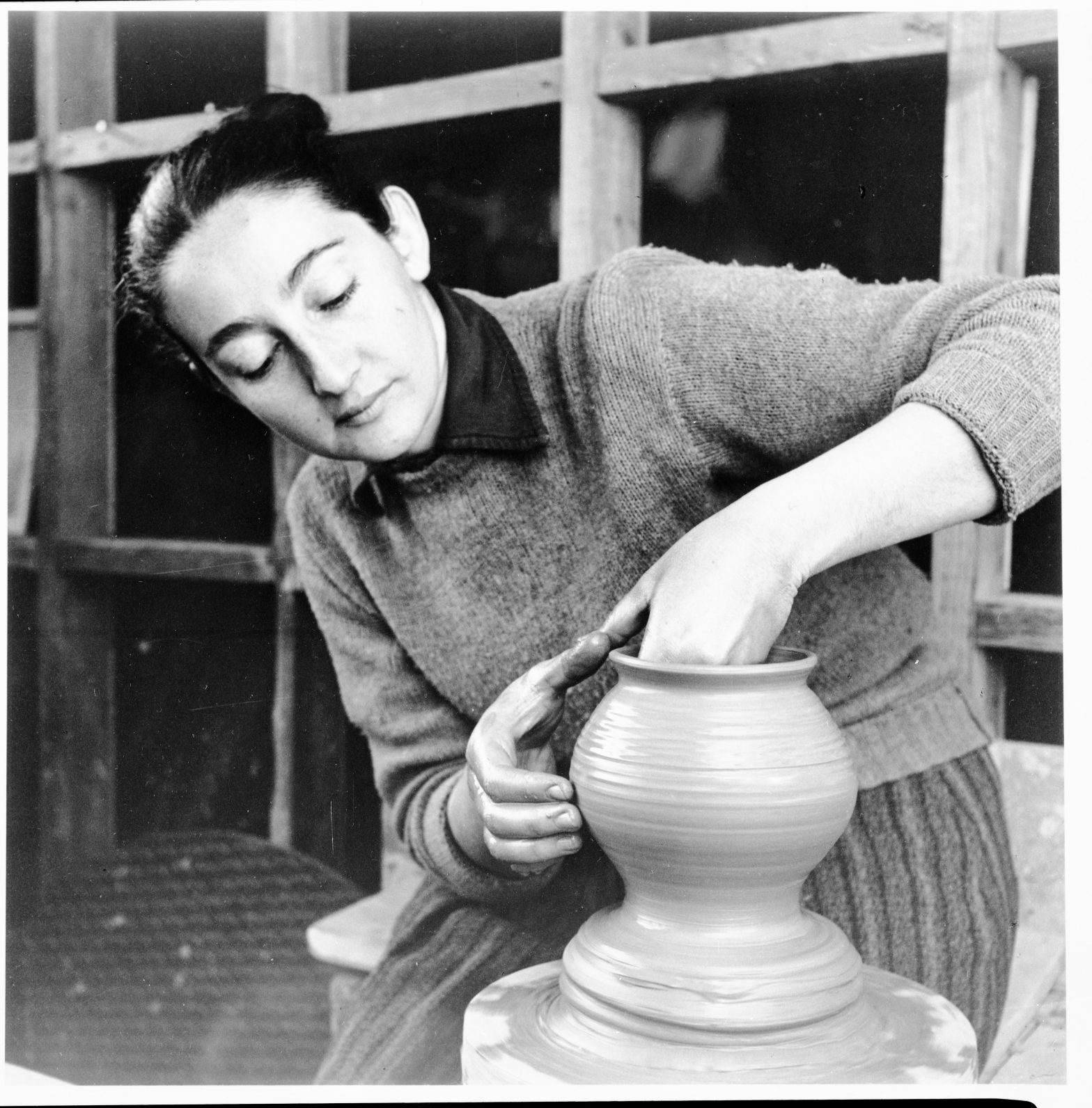 Black and white photo of a white woman working on a ceramic pot on a pottery wheel.