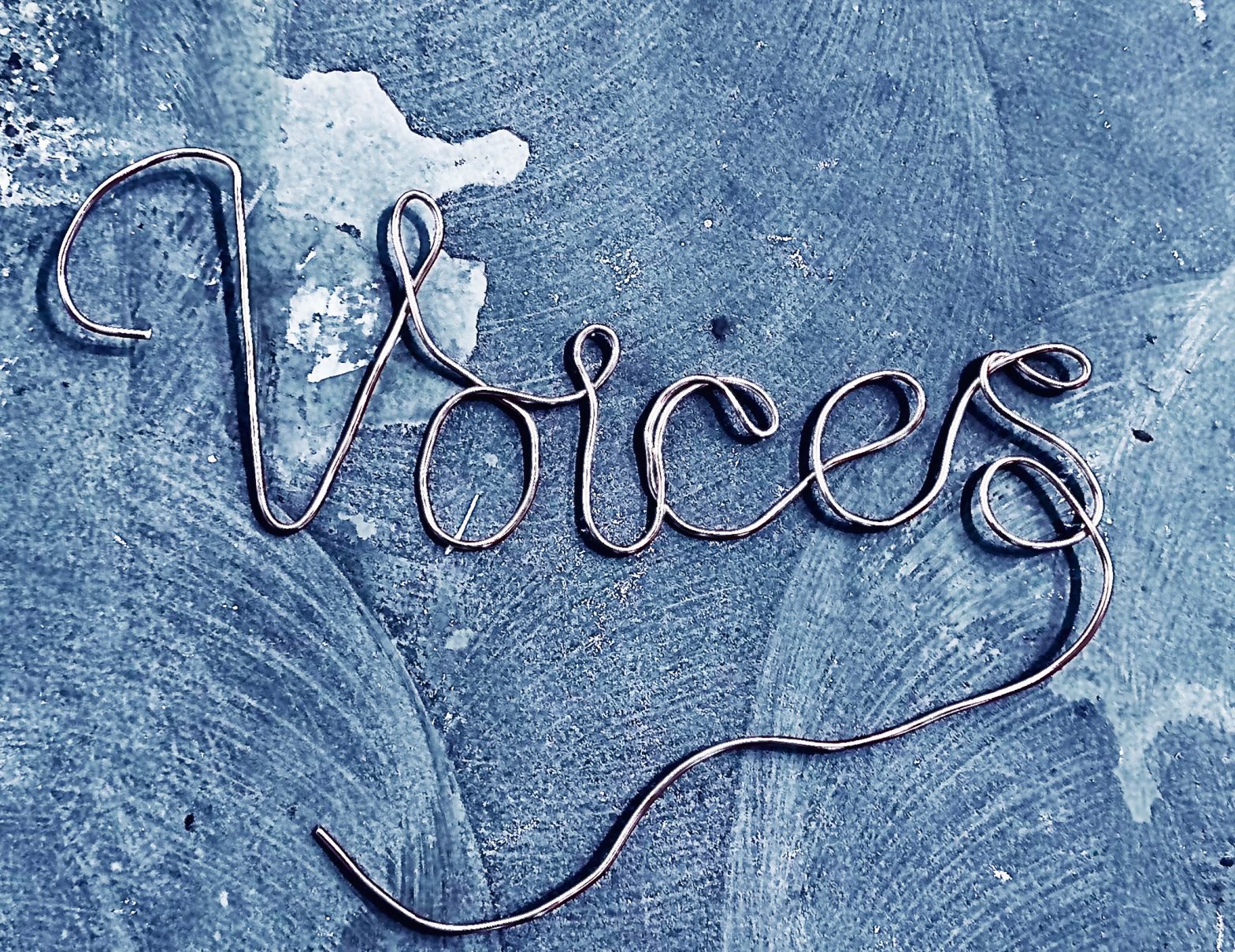 The word Voices made from wire against a floor or surface with patches of brushwork and watermarks.