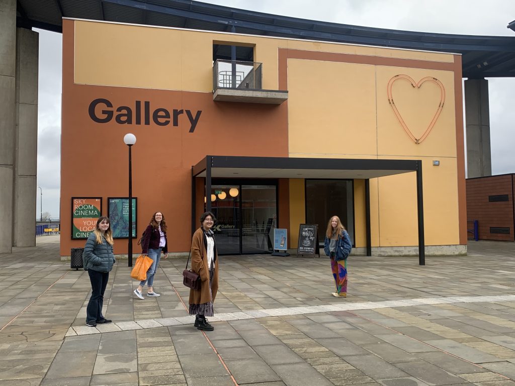 Four people standing posing outside a large brown and cream building with the words 'Gallery' in large letters.