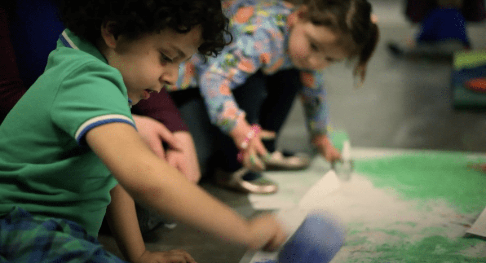Two toddlers playing with sand and paint on paper.