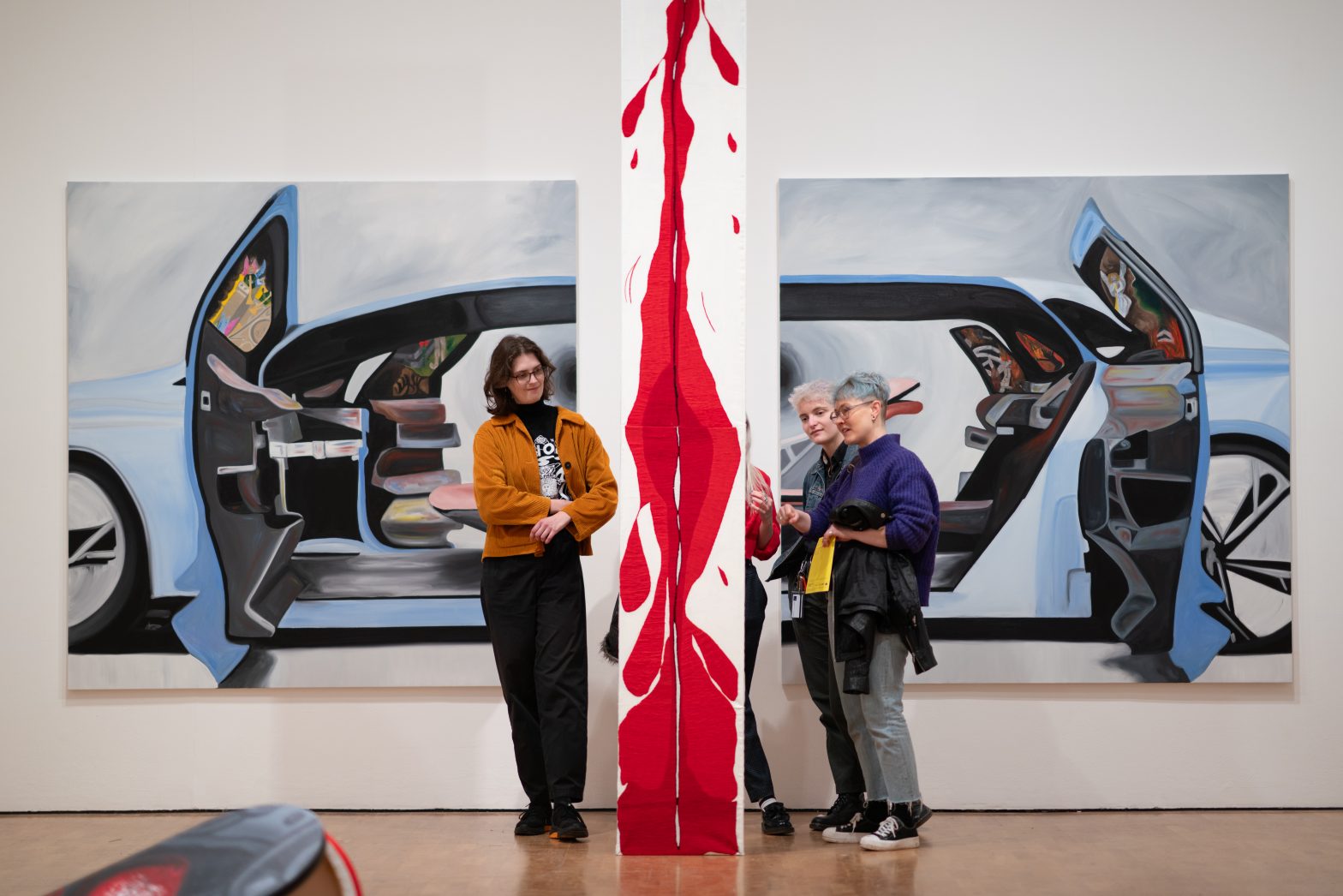 3 people stand admiring a bright red embroidered artwork by Frieda Toranzo Jaeger.