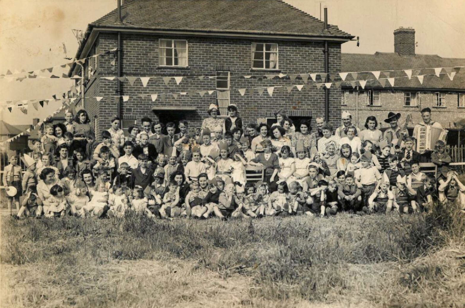 Celebratory black and white group photo from 1953 of many people outside a brick building with bunting strung up.