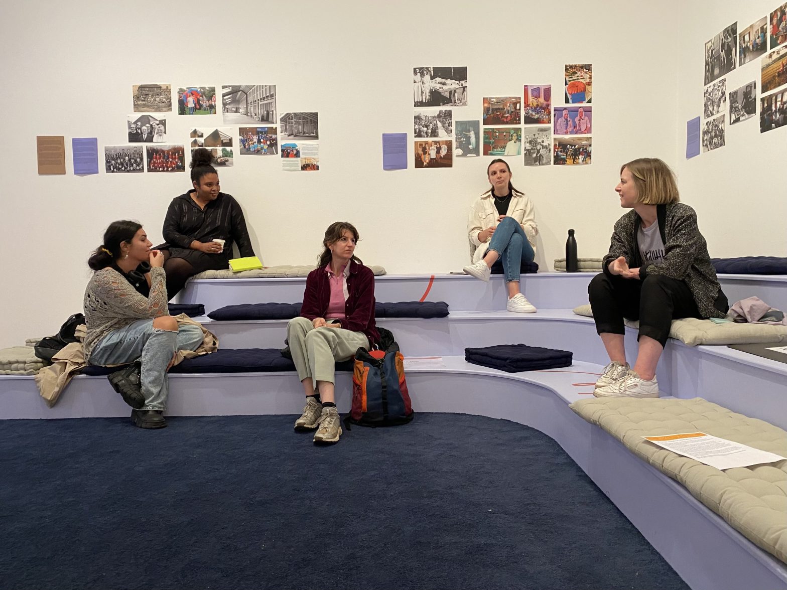 A group of people sit on lilac benches at different heights.