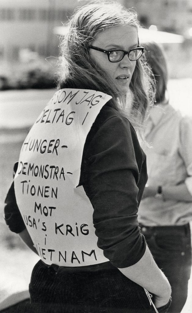 Monica Sjöö protesting the Vietnam War in Stockholm. She wears a piece of a paper with writing pinned to her back. 