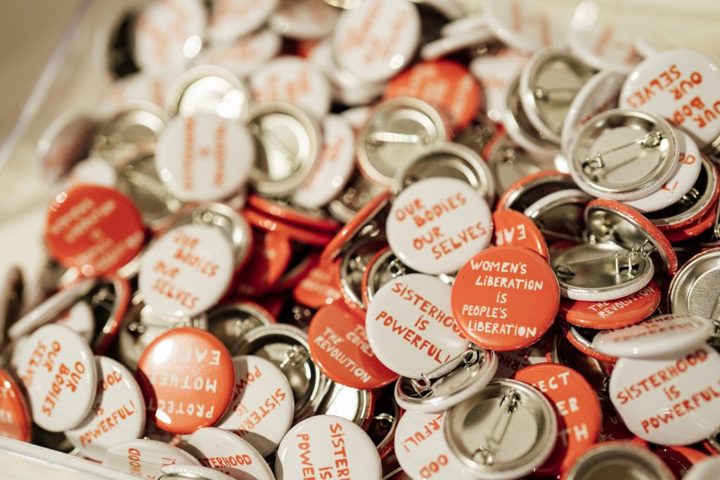 Photograph of orange and white badges with feminist slogans printed on them.