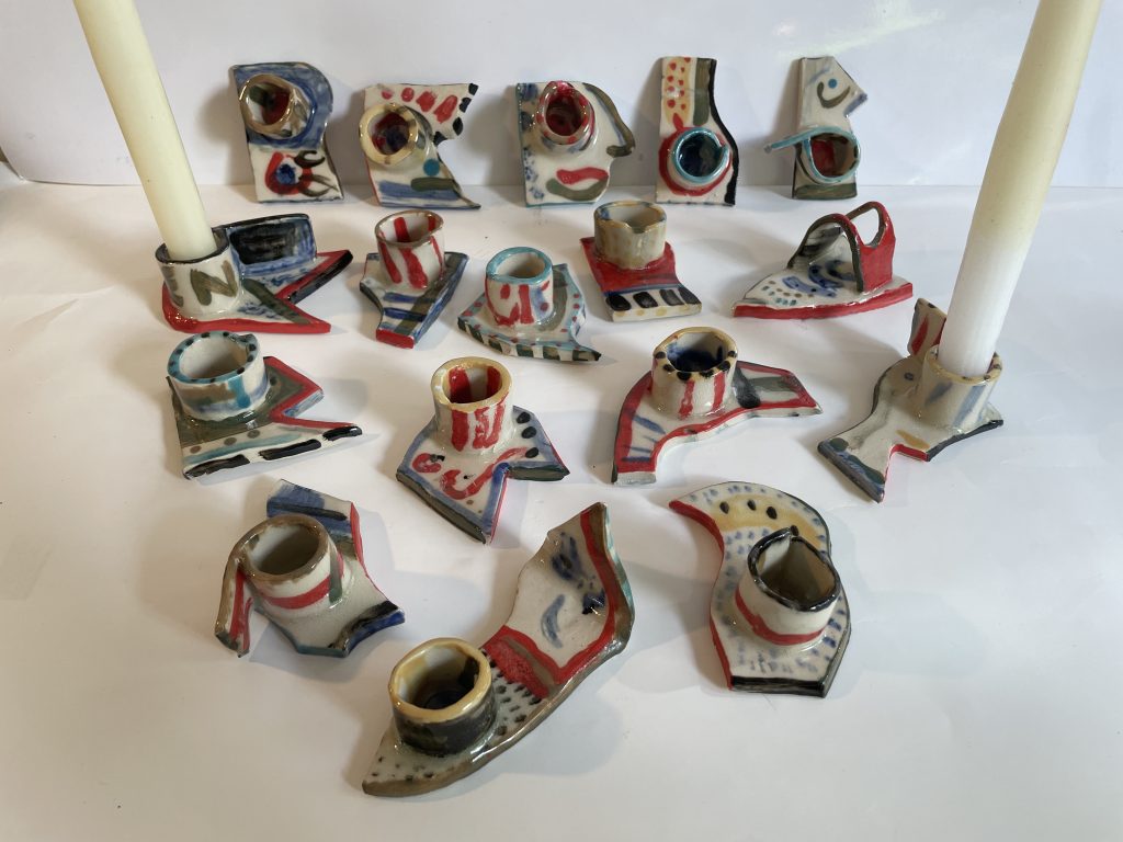 Photograph of ceramic candle holders, decorated with stripes and. spots in sahdes of black, yellow, blue and red.