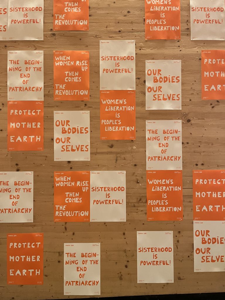 Photograph of bright orange and white posters bearing feminist slogans.