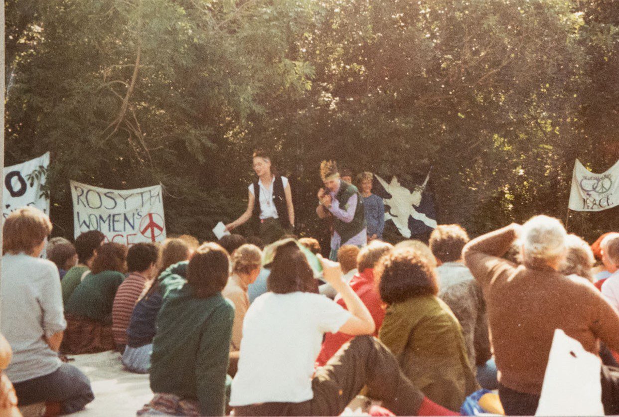 A photograph of women forming a blockade, as described in the Green Gate Podcast. A number of banners hang from trees and bushes.