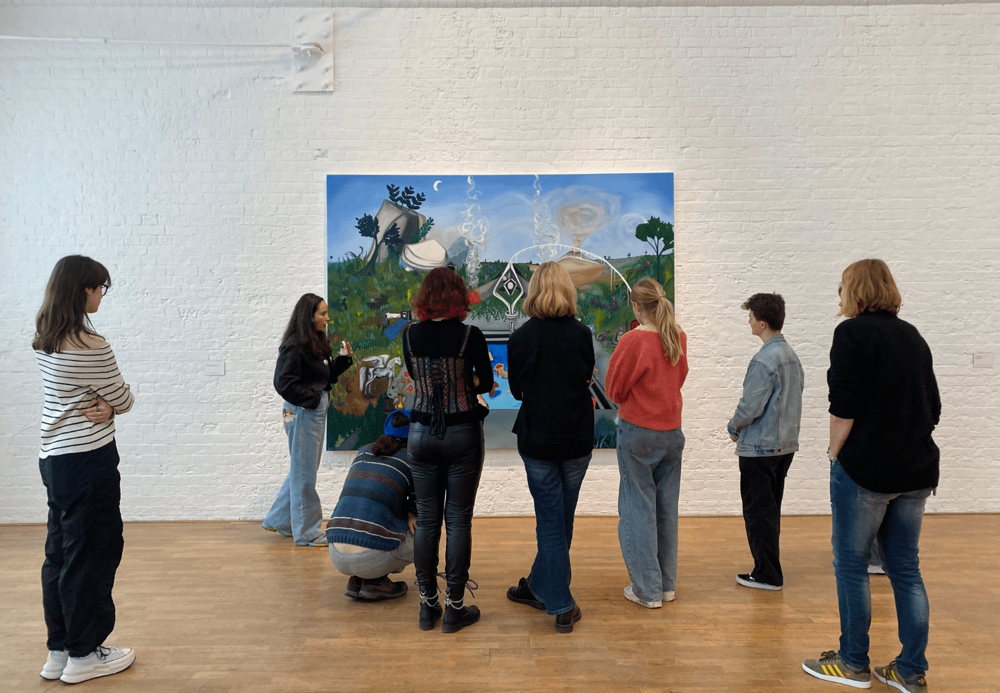 A group of young people are gathered around a painting by Frieda Toranzo Jaeger in an large bright art gallery