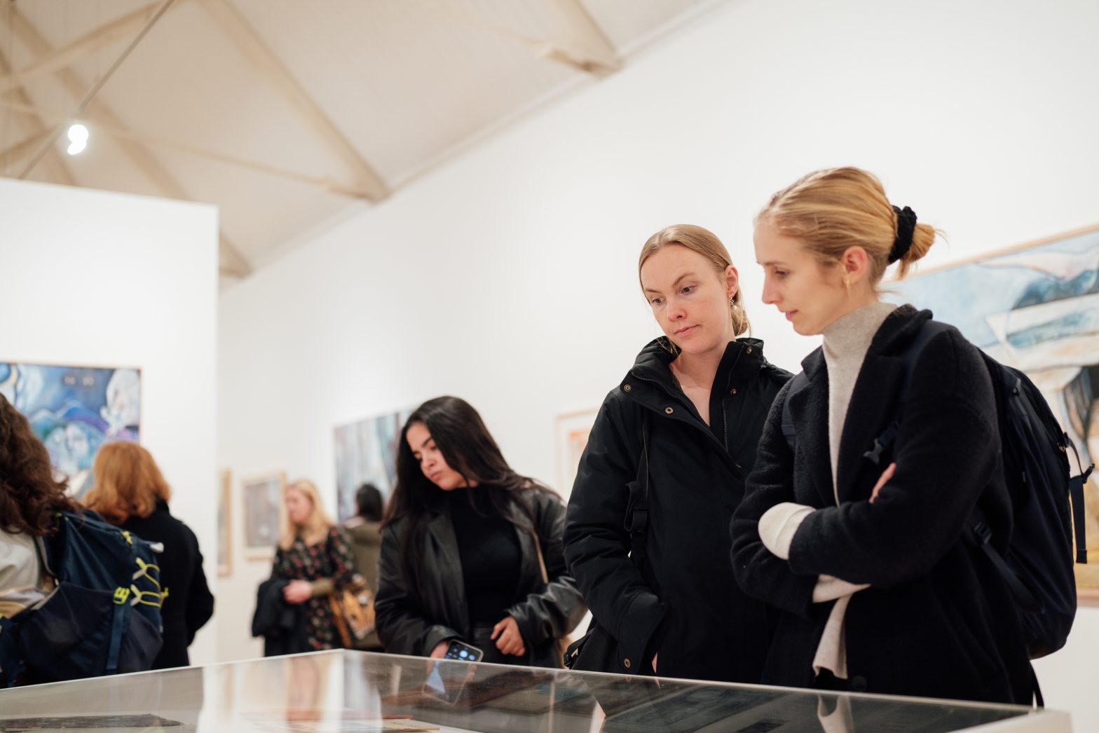A group of people in an art gallery being shown a piece of art in a tour. They are all looking towards the bottom left corner.