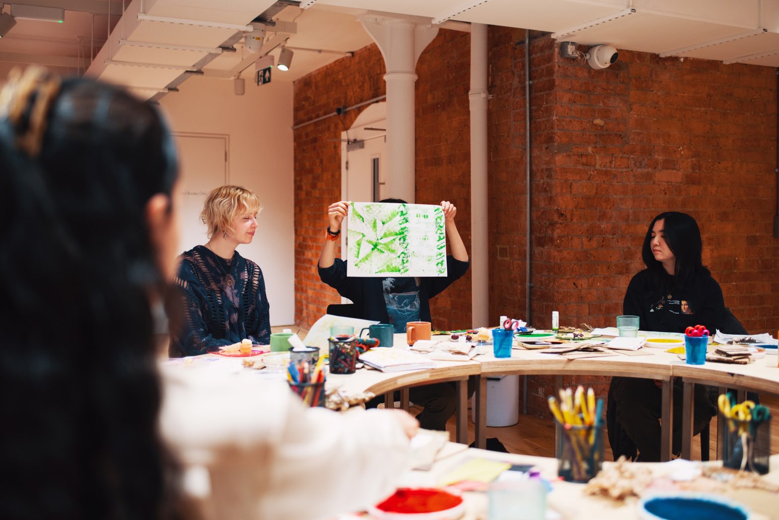 A photo of a workshop happening in Modern Art Oxfords Creative Space. Young people are sat around a table showing each other their creations.