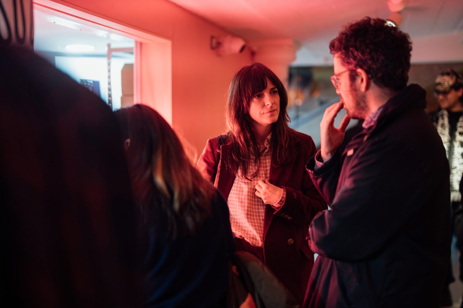 Two people stand talking, illuminated by a pink glowing light.