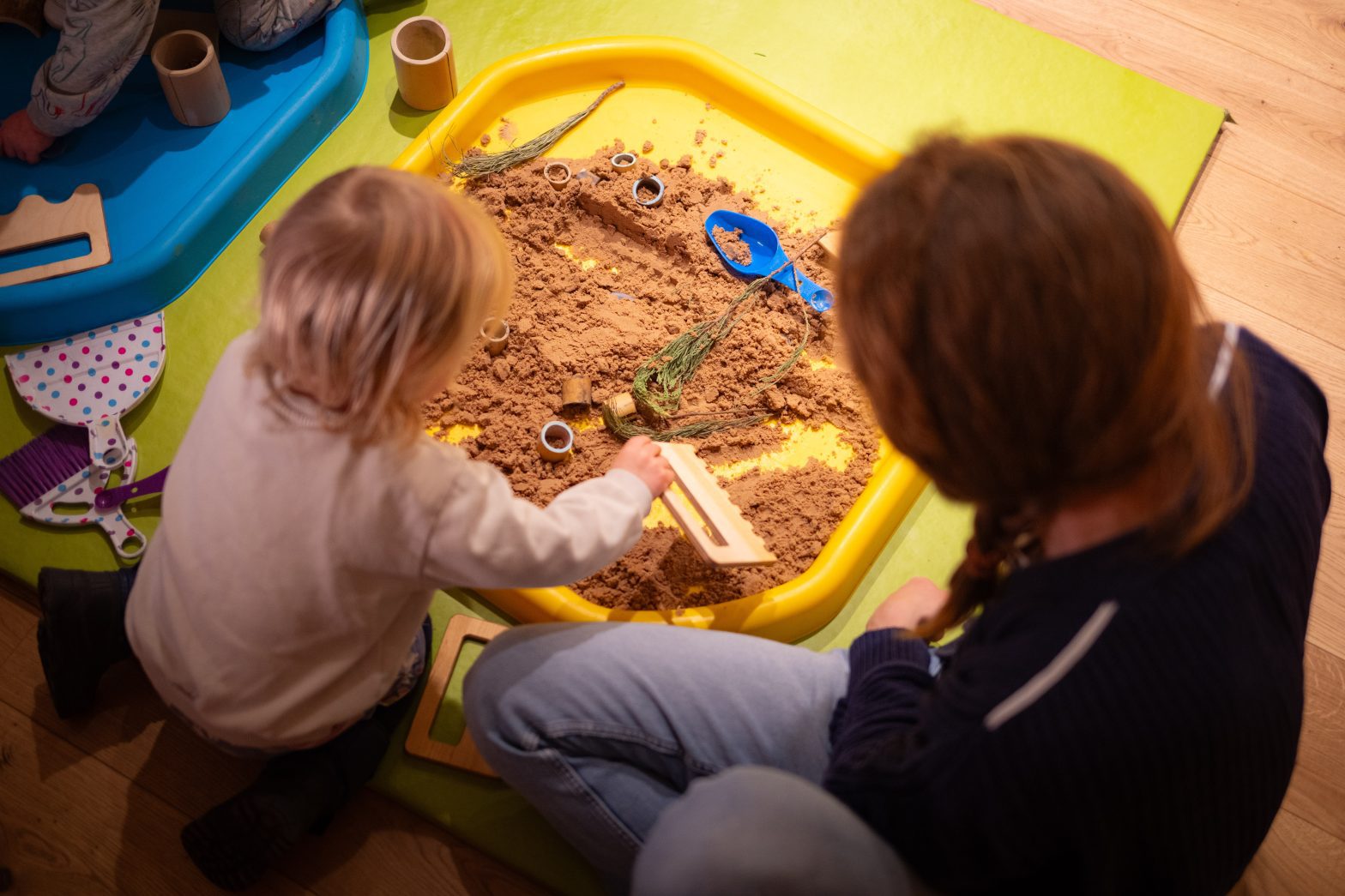 A parent and child play in a sand box.