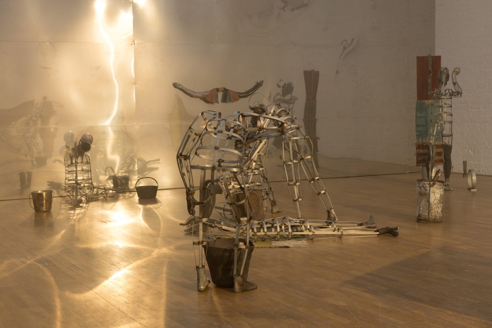 installation image of Kira Freije: Unspeak the Chorus at Modern Art Oxford. It shows metal figures posed in a gallery with light shining over them.