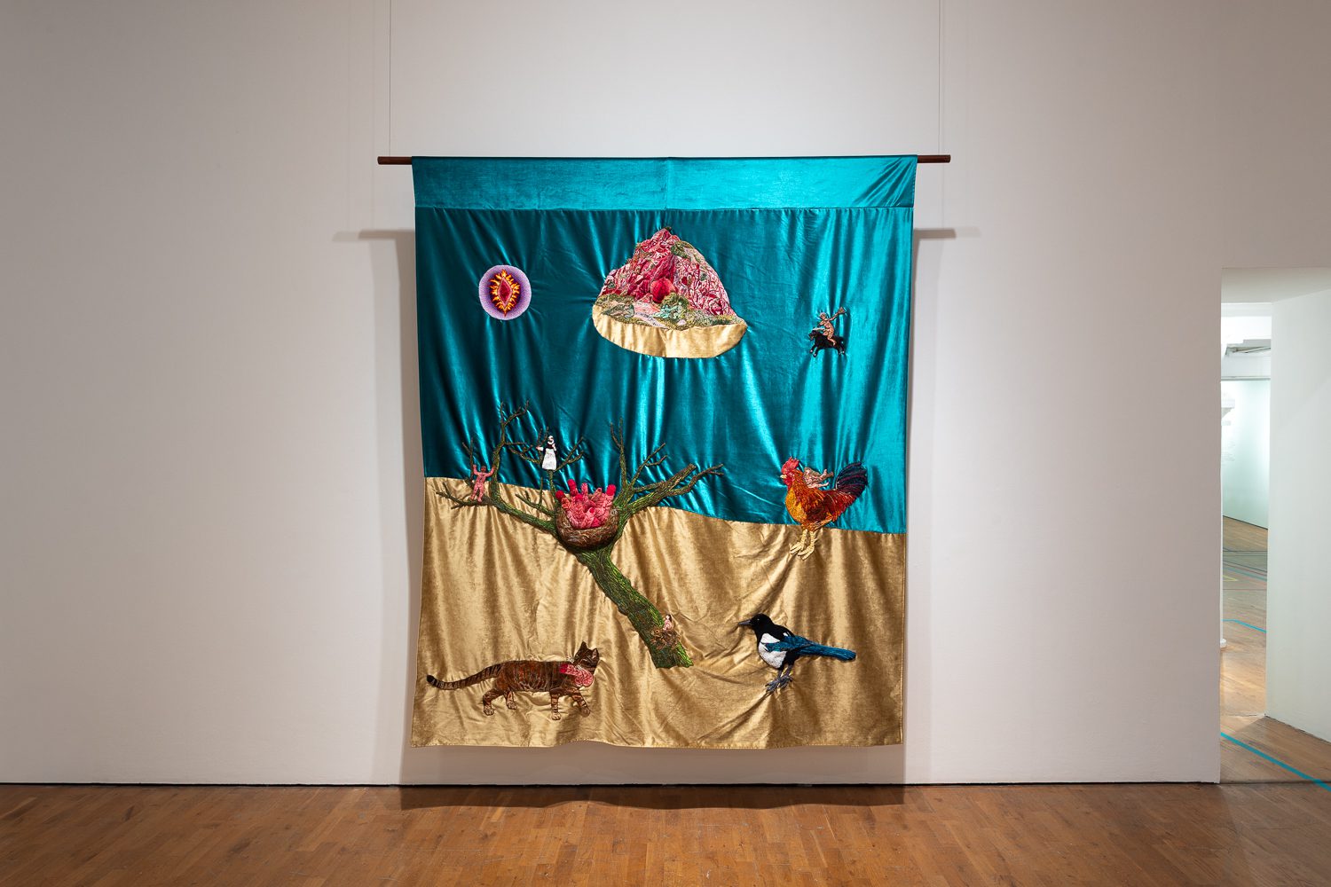 Installation view of Olivia Plender: Little Fennel's Complaint on show at Modern Art Oxford. It features a tapestry of embroidered animals and figures exploring the Witch Craze.