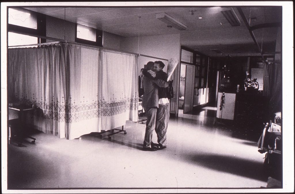 One of the photos featured in Positive Lives Exhibition at Modern Art Oxford (1994). It shows two people hugging in a hospital holding flowers. 