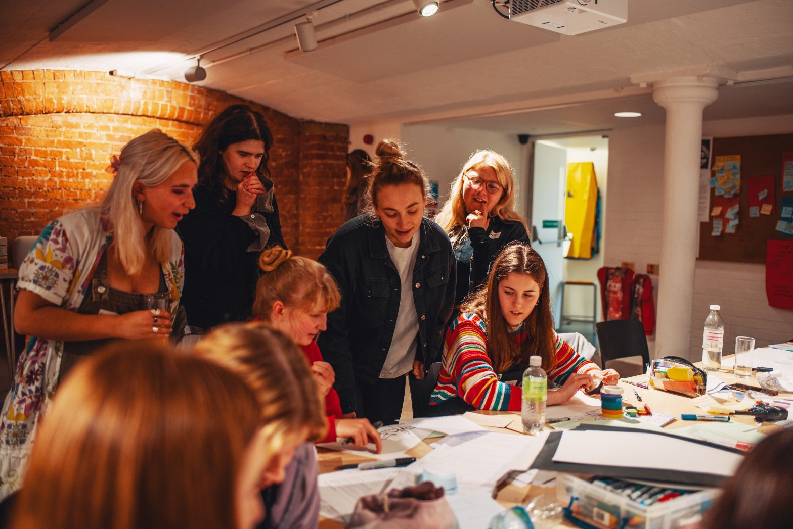A group of young people huddled around a table, looking at a creative project together.