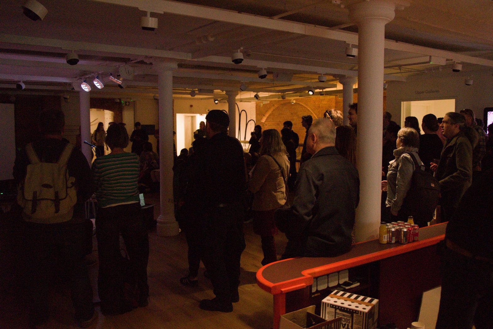 A group of people gathered in watching a performance in a room with low ceilings and pillars at Modern Art Oxford.