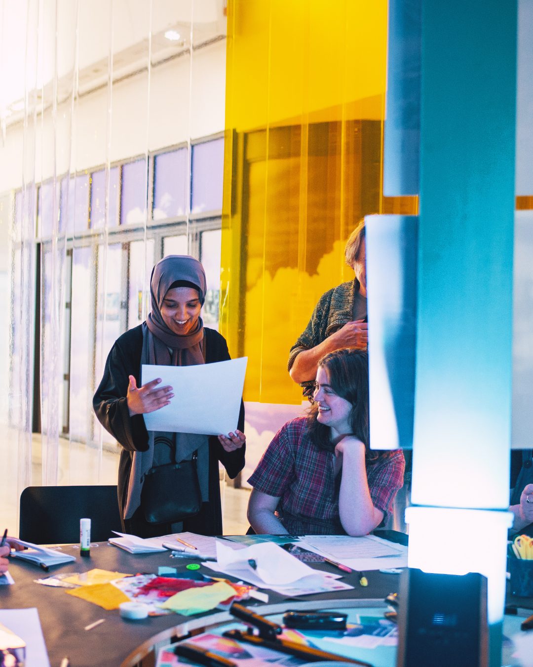 A photo of two women smiling looking through papers on a workshop table.