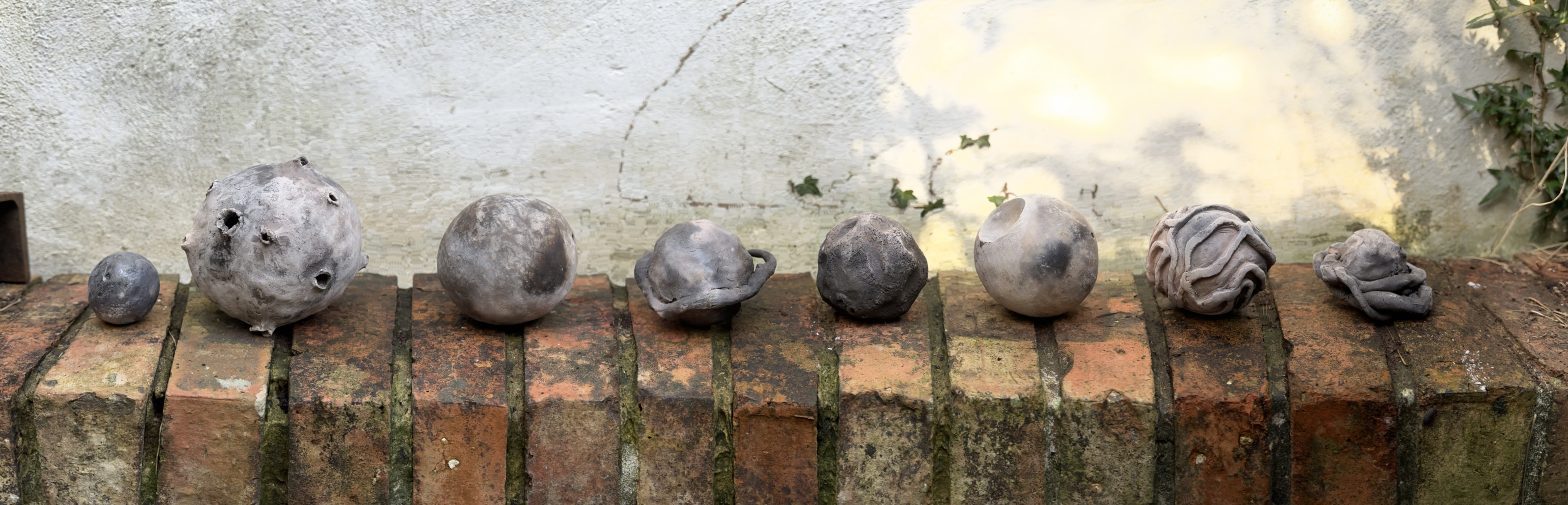 Hand made clay spheres (planets) are lined up on a brick wall